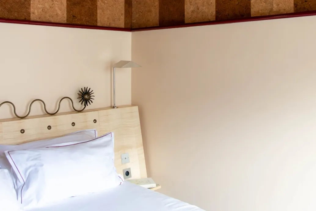 Aperçu réduit d'un coin de lit aux draps blancs, adossé à un mur clair sous une frise de liège.