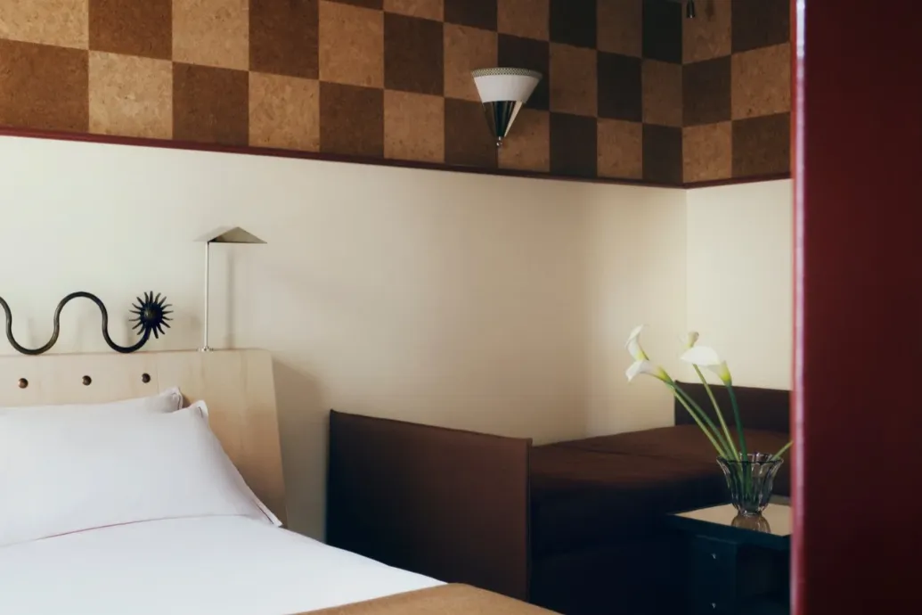 Aperçu d'une chambre au décor rétro, avec un lit blanc, une banquette brune et un plafond en damier de liège.