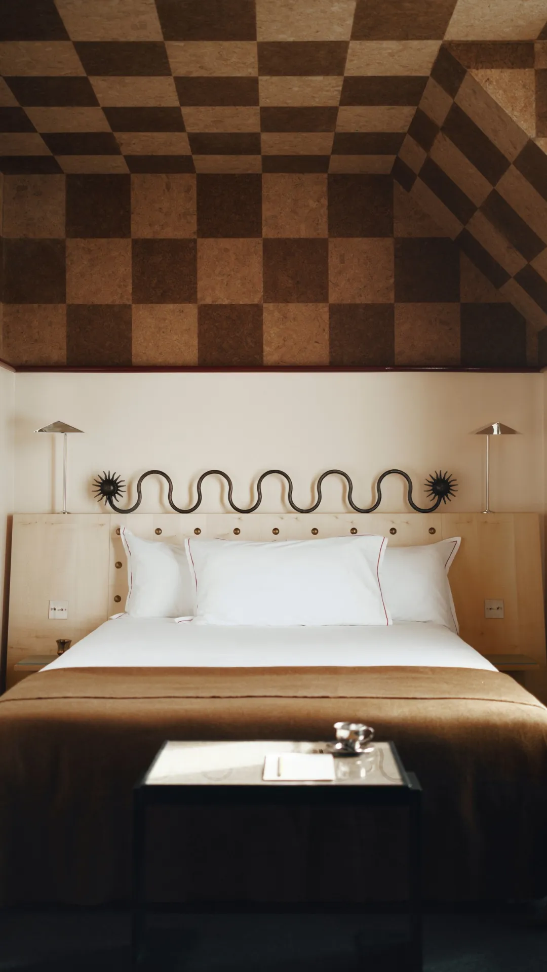 Chambre design à Montmartre vue de face, lit blanc, plaid camel et plafond en liège à damier de l'Hôtel Luxia