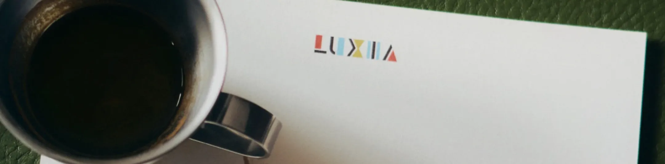 Black coffee cup top view placed on a white sheet with the colorful Luxia logo on a textured green surface.