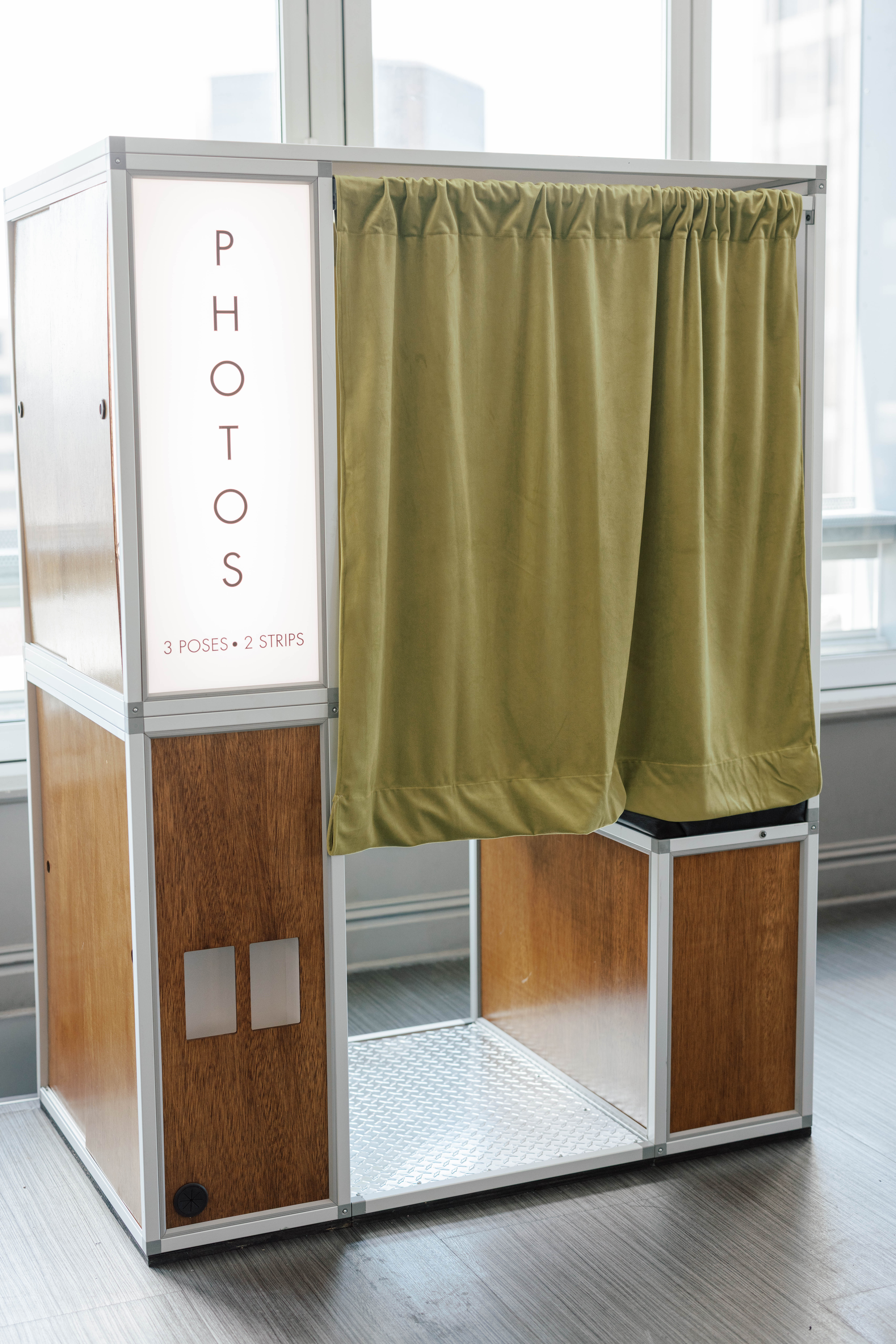 Photo booth with light-up sign reading PHOTOS 3 poses 2 strips and green curtain entrance.