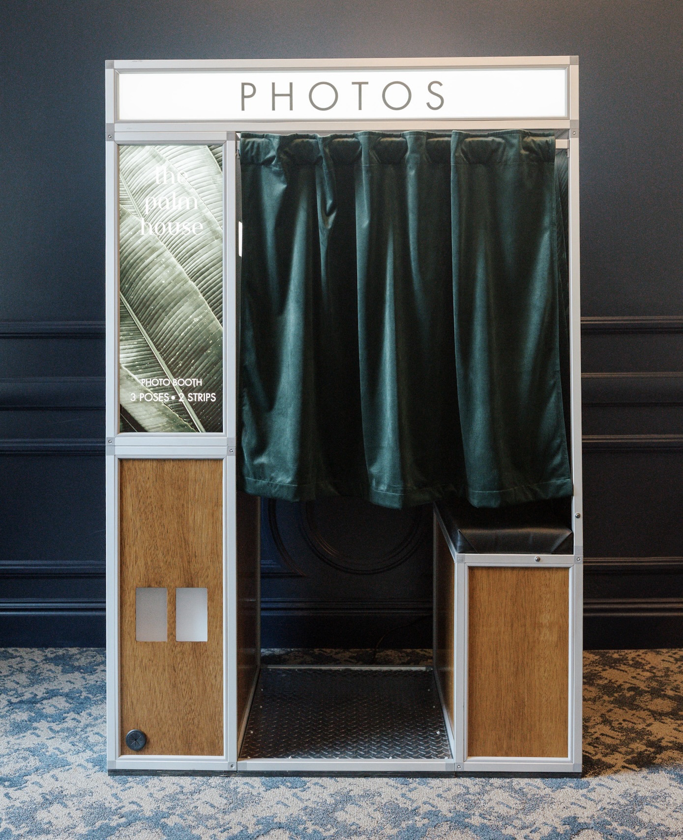 Vintage photo booth with closed dark green curtain and wood panels on a patterned carpet.