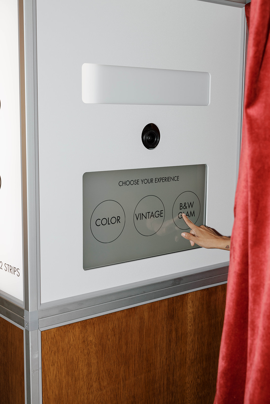 Hand selecting B&W Glam option on a photo booth touch screen labeled Choose Your Experience.