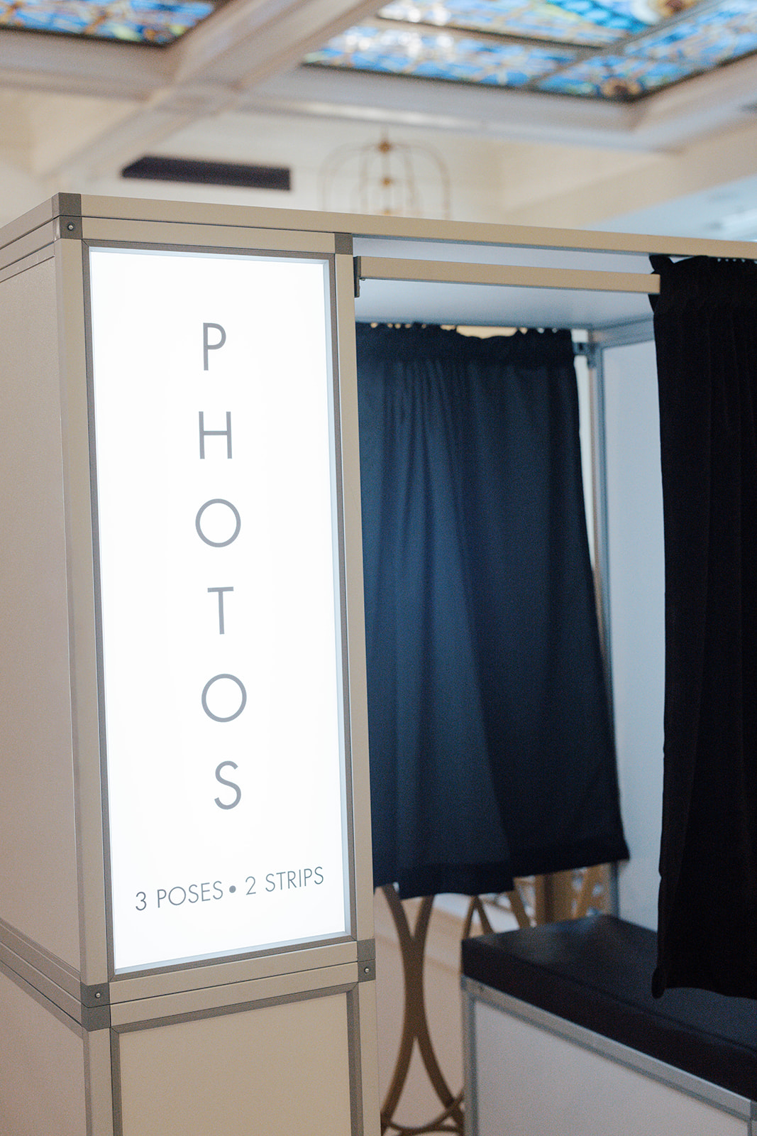 Photo booth with black curtains and a sign reading 'PHOTOS 3 poses 2 strips'.
