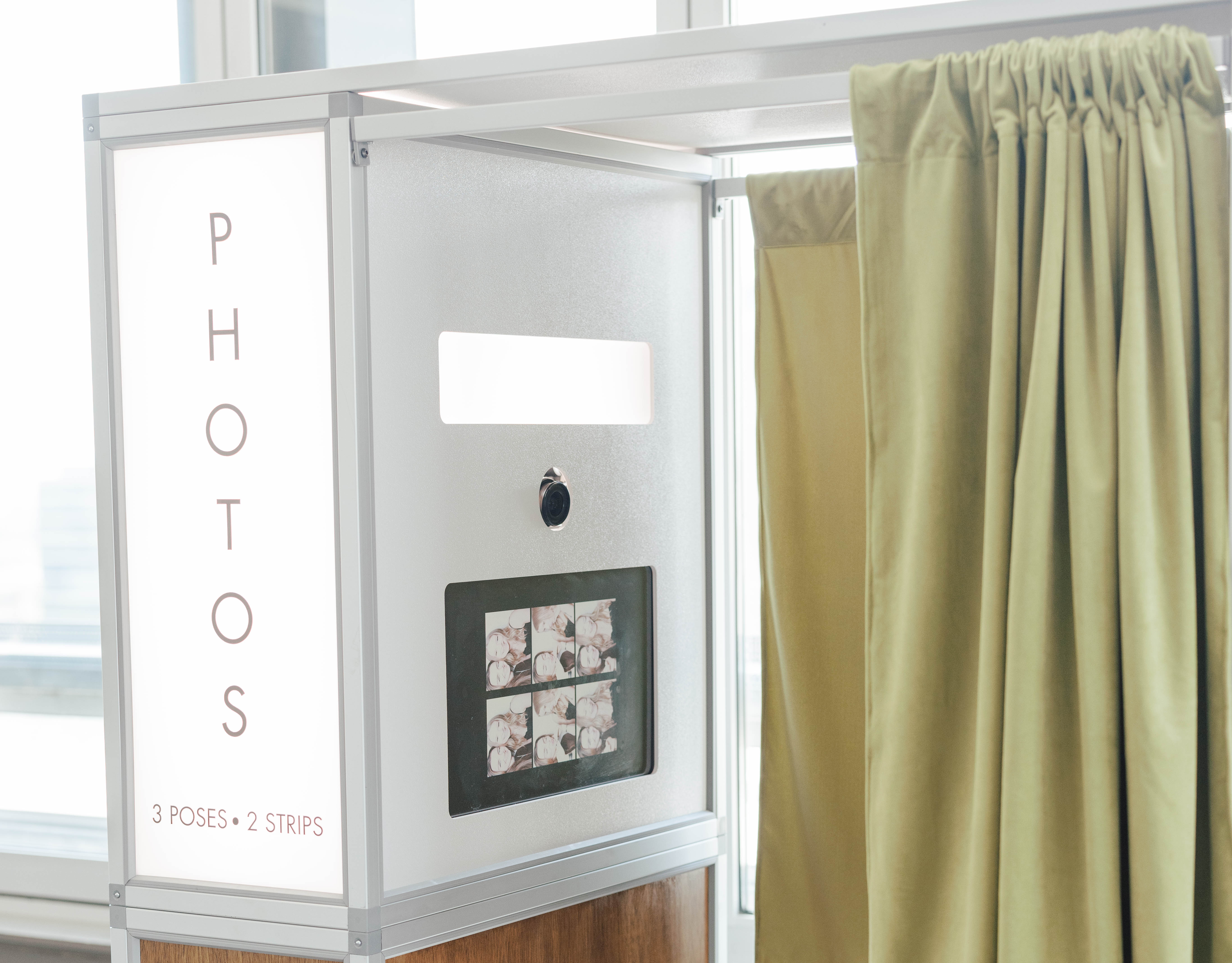 Photo booth with a camera, photo strips display, and olive green curtain.