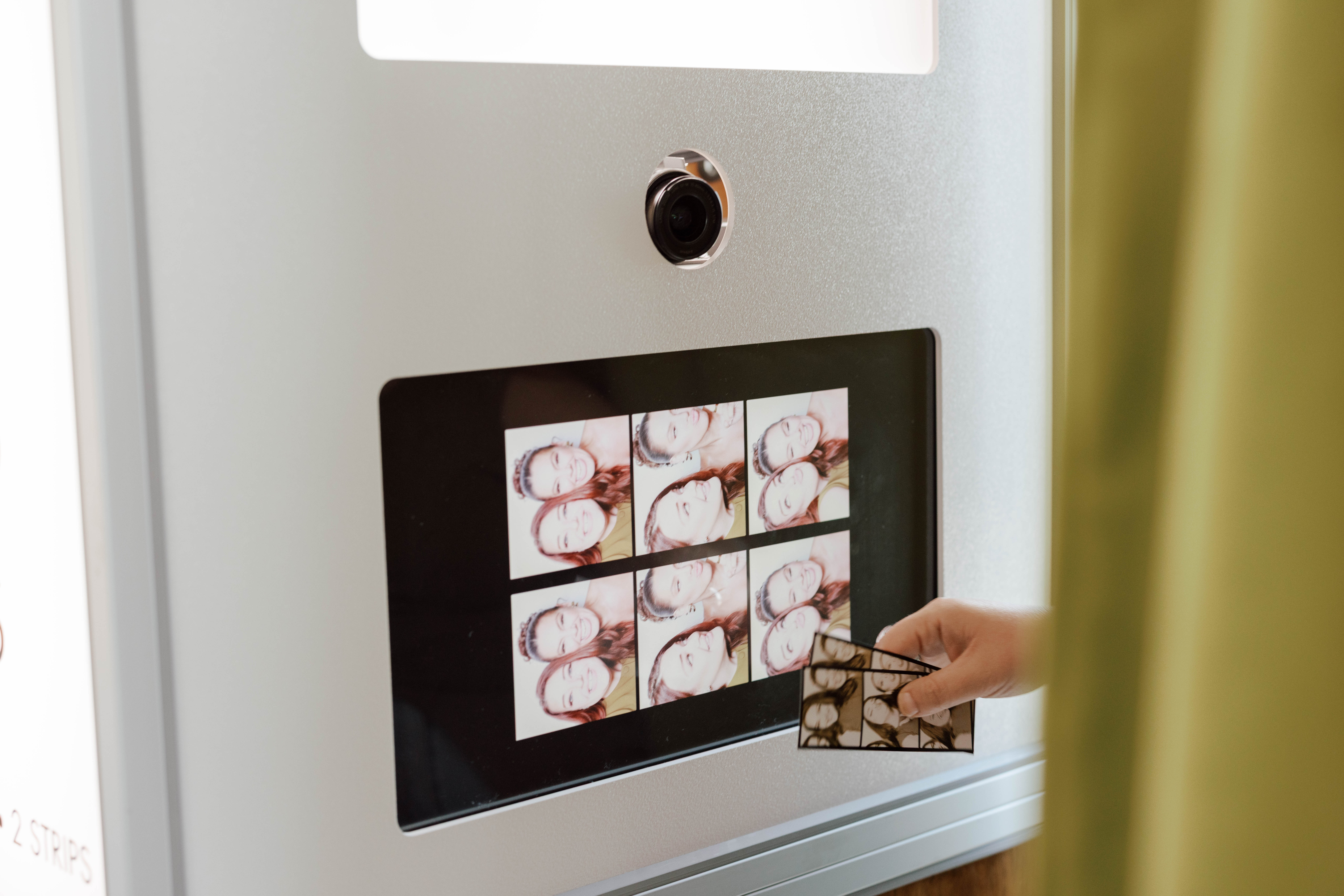 Hand holding photo booth strips showing smiling women displayed on a photo booth screen.