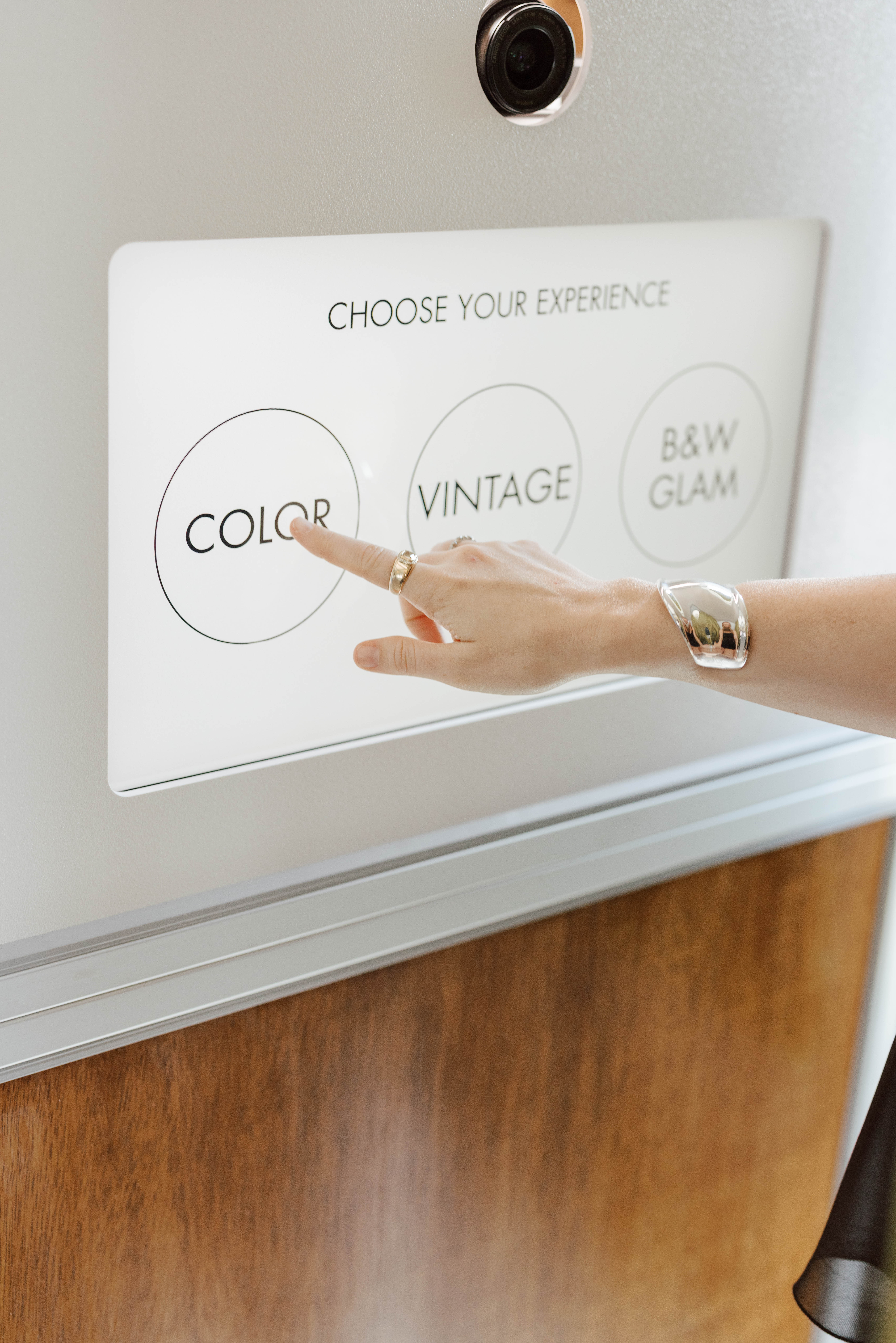 Hand with rings and bracelet selecting 'COLOR' option on a touch screen with three photo style choices.