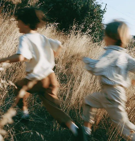 Two children running through a dry grassy field on a sunny day.