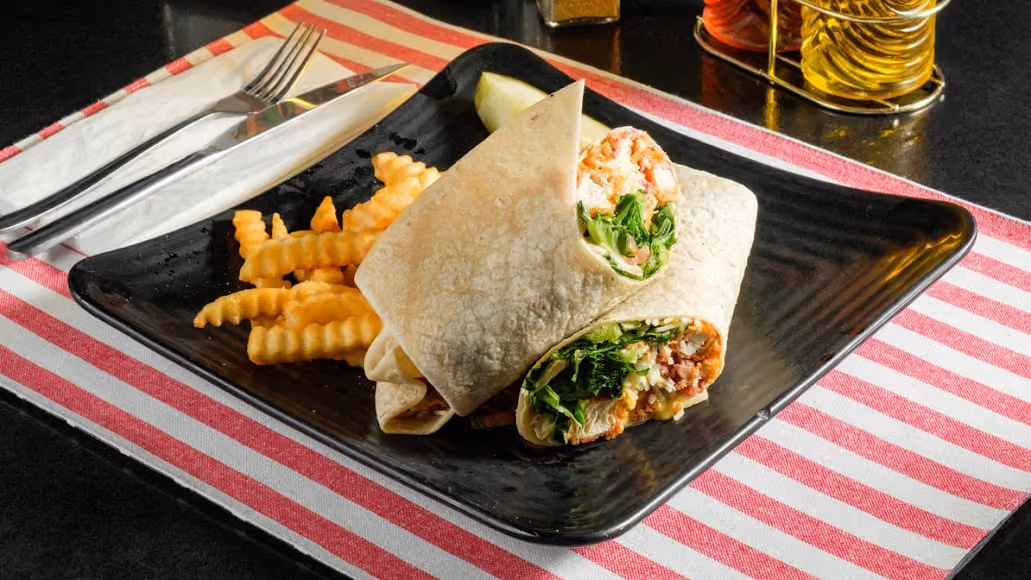 Wrap sandwich halves with lettuce and filling, served with crinkle-cut fries on black plate.