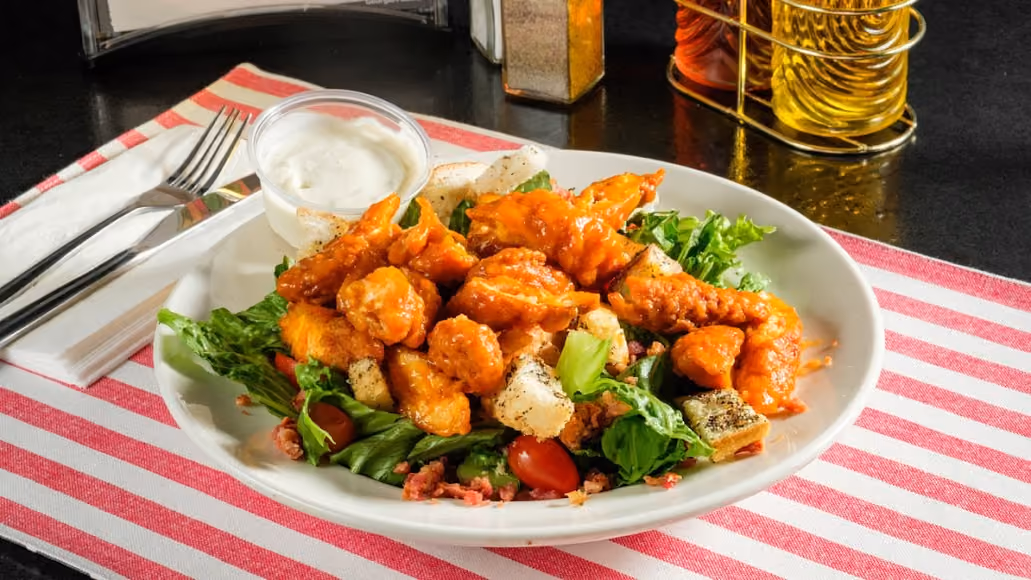 Buffalo chicken salad with lettuce, cherry tomatoes, croutons, and a side of ranch dressing.