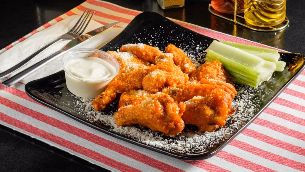 Plate of buffalo chicken wings with ranch dressing and celery sticks on a striped cloth napkin.