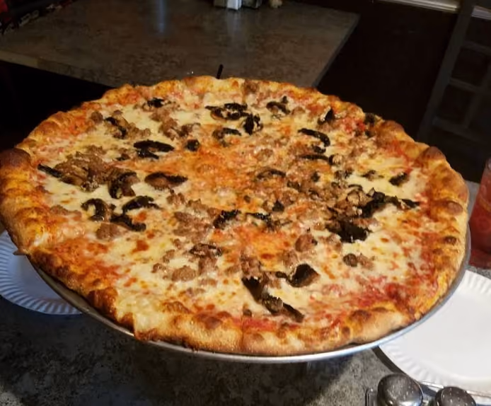 Large pizza with cheese, mushrooms, and sausage on a metal stand in a restaurant setting.
