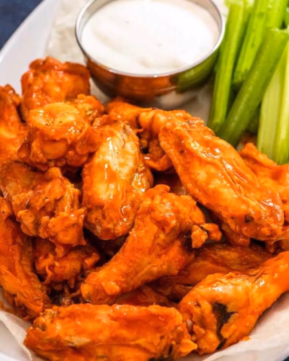 Plate of buffalo chicken wings with celery sticks and a cup of dipping sauce.