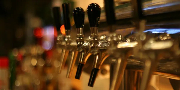 Close-up of several beer taps with black handles in a dimly lit bar setting.