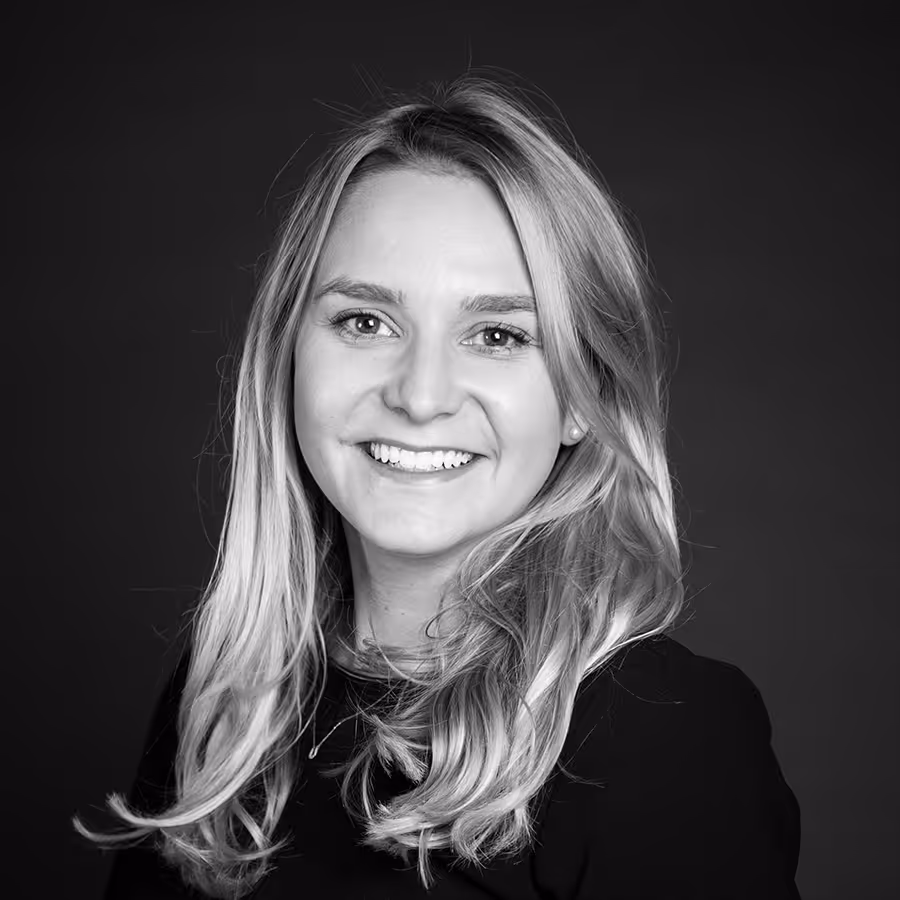 Porträt einer lächelnden Frau mit langen blonden Haaren vor dunklem Hintergrund.