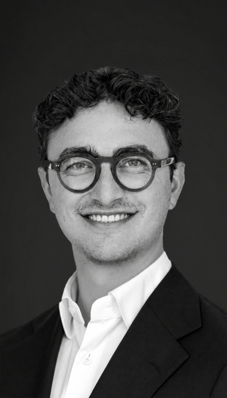 Porträt eines Mannes mit kurzen braunen Haaren, Brille, weißem Hemd und dunkelblauem Sakko.