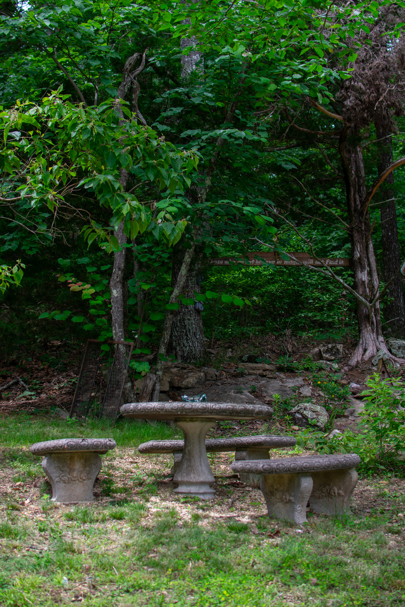 Round stone table with four curved stone stools in a leafy green forest clearing.