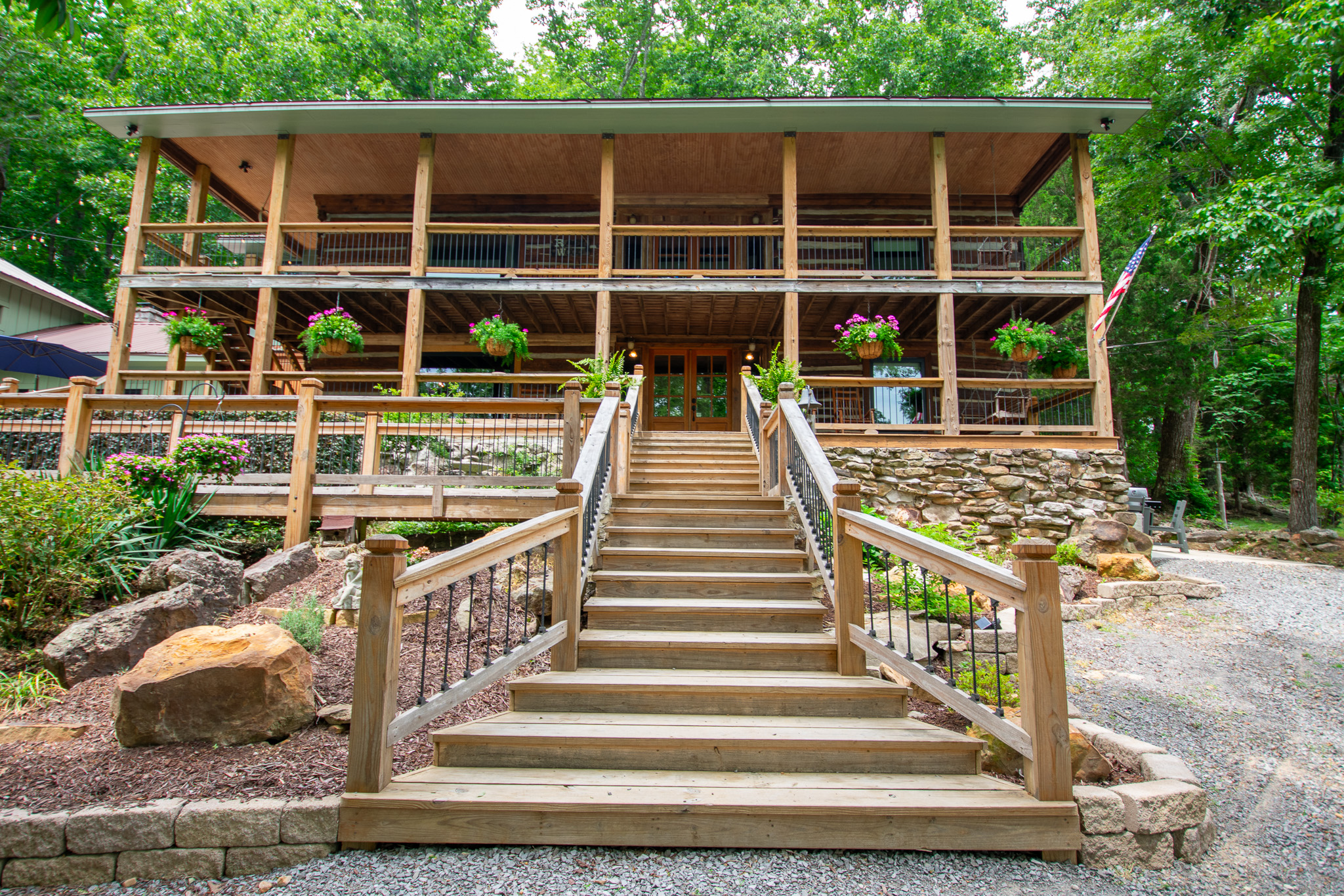 Front view of a wooden house with two covered porches and stairs lined with flower pots and plants.