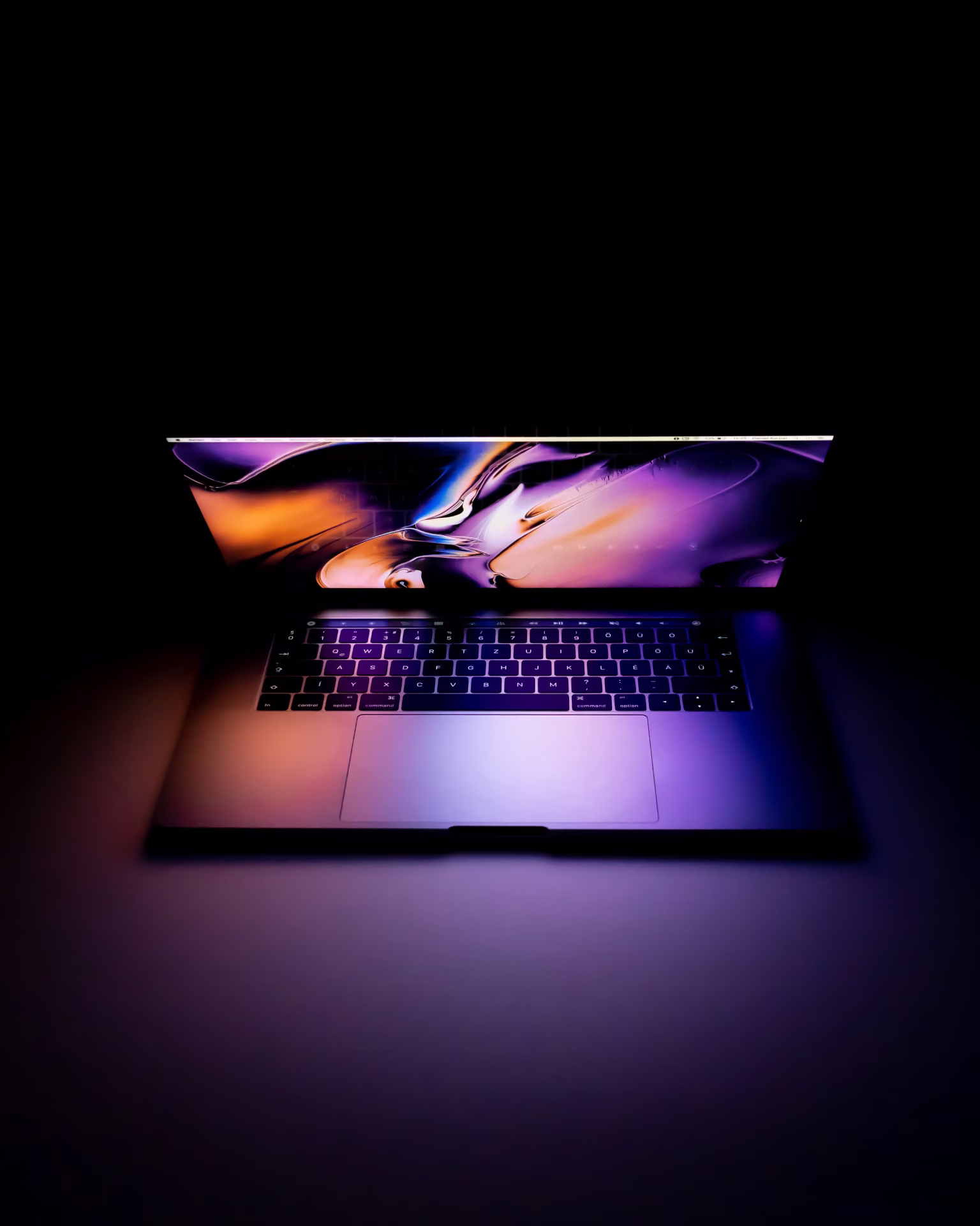 Laptop with illuminated colorful abstract screen and keyboard in a dark environment.