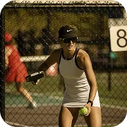 Woman in white sportswear preparing to hit a tennis ball on an outdoor court at sunset.
