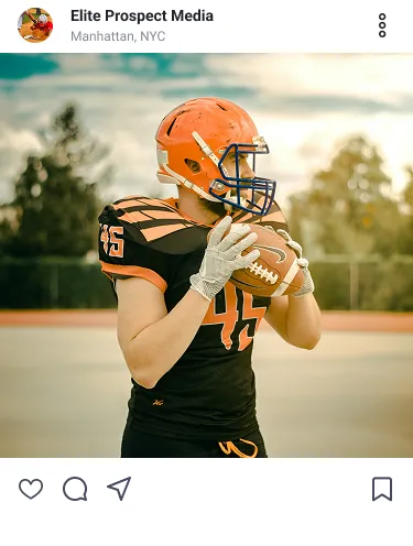American football player in black and orange uniform holding a football on a field at sunset.