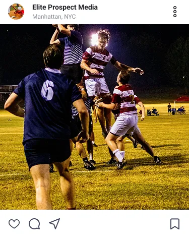 High school soccer players compete for a header during a night game on a grass field.