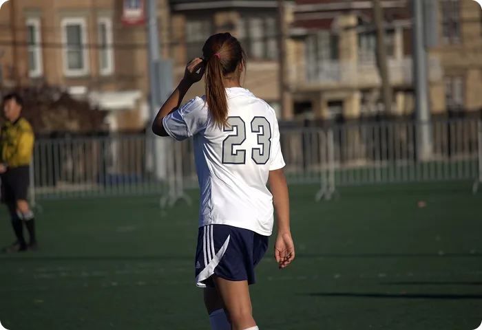 Female soccer player wearing number 23 jersey walking away on a sports field with a referee in background.