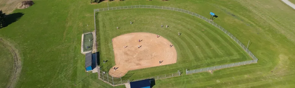 Aerial view of a baseball field with players on the diamond and green grassy outfield.
