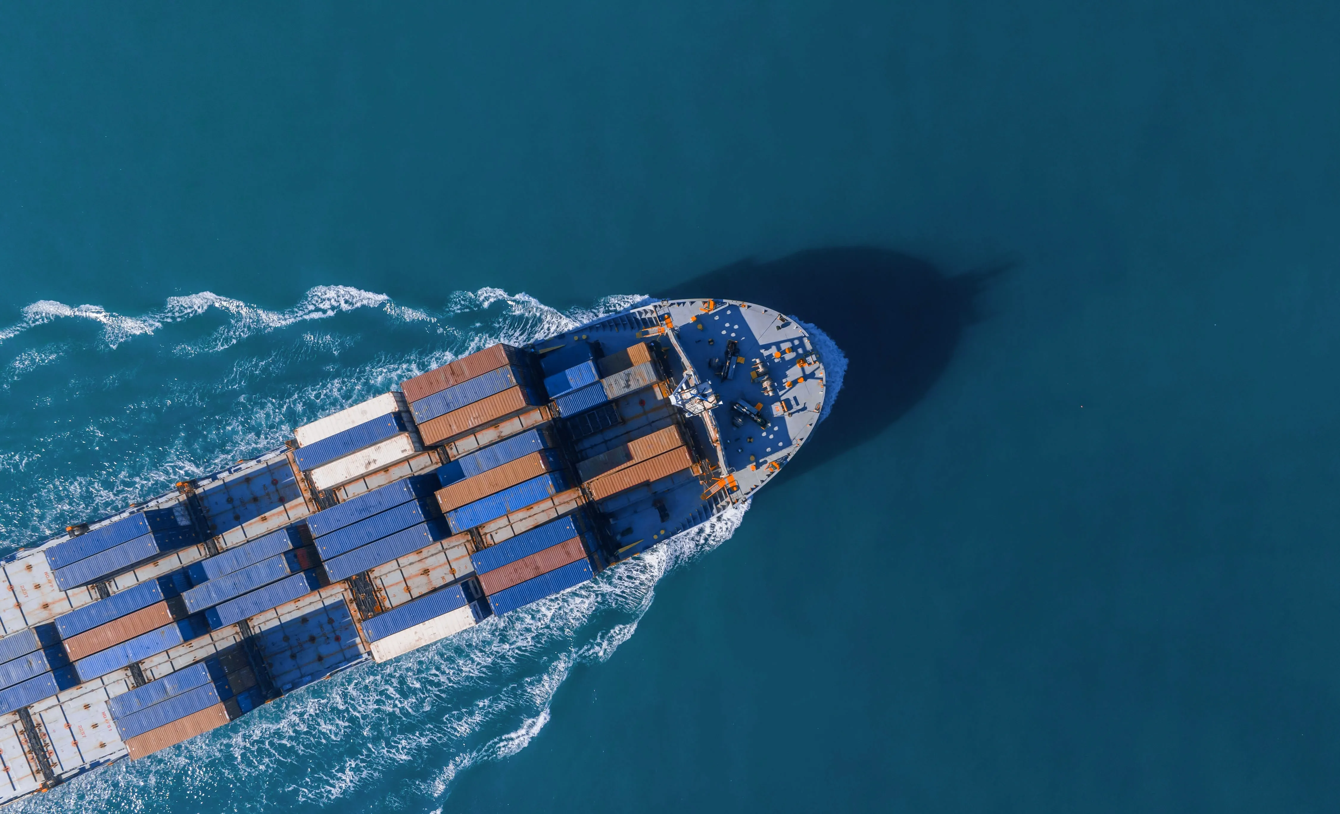 Aerial view of a cargo ship carrying multicolored containers sailing on open ocean water.