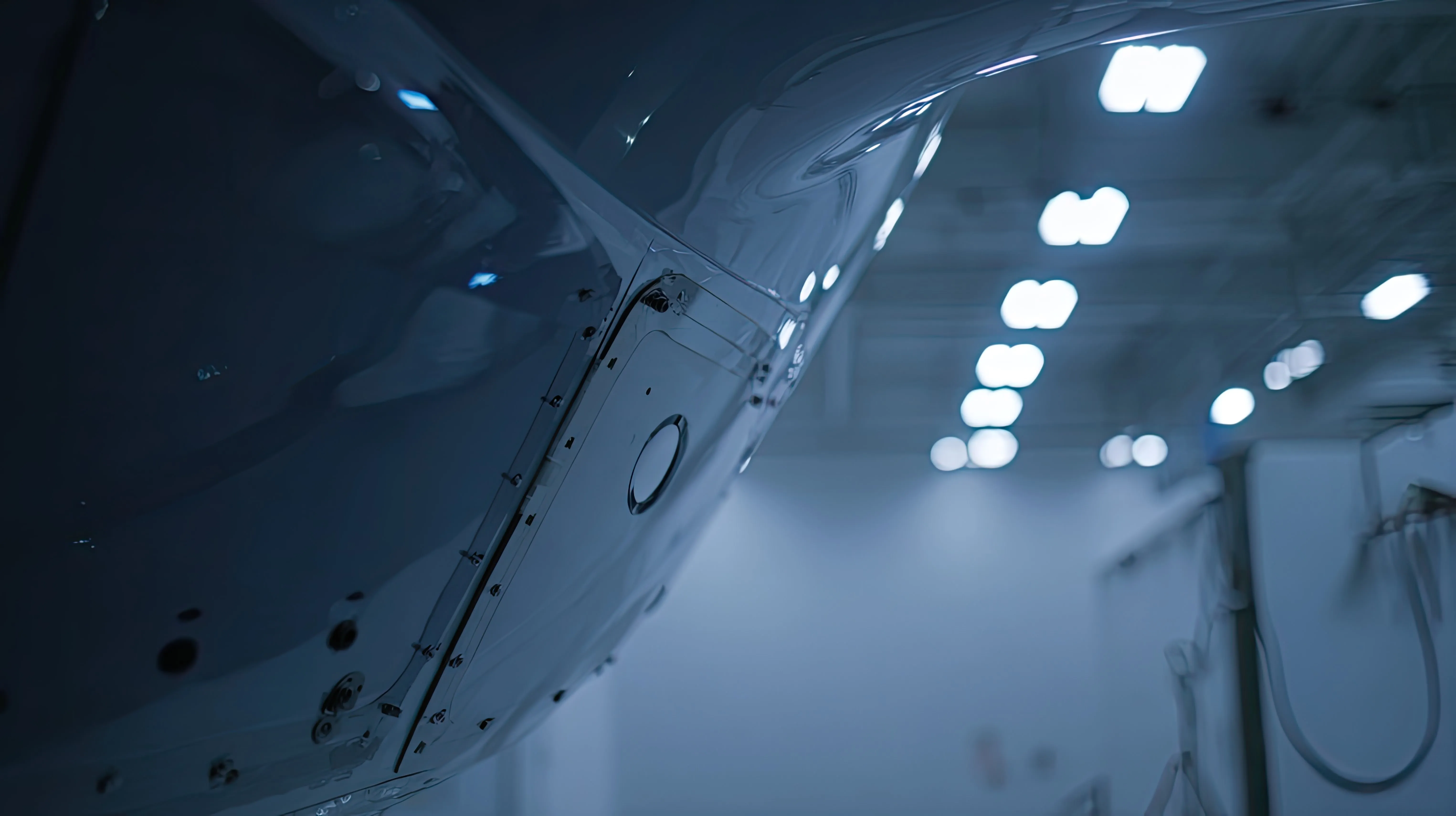 Close-up of a sleek aircraft surface in a bright, modern hangar with lights reflected on it.