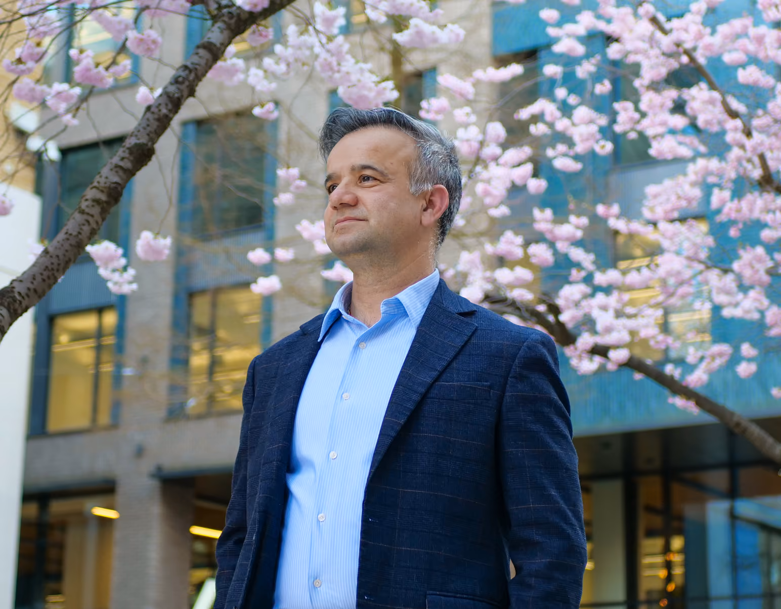 Business leader in a navy blazer standing outside an office building under cherry blossom