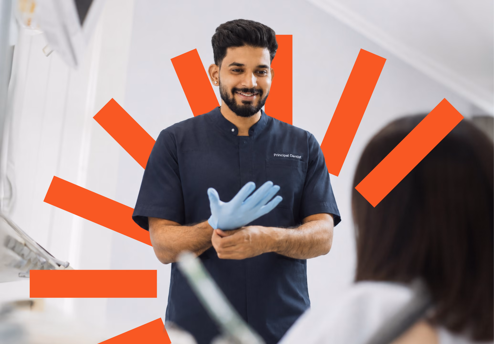 Smiling man in dark scrubs and blue gloves in front of an orange sunburst wall graphic