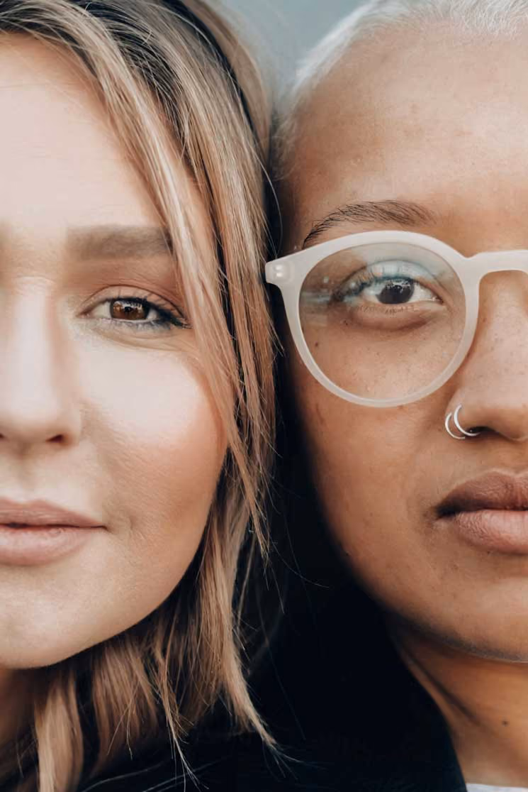 Close-up of two diverse women’s faces side by side, one with glasses and nose rings.