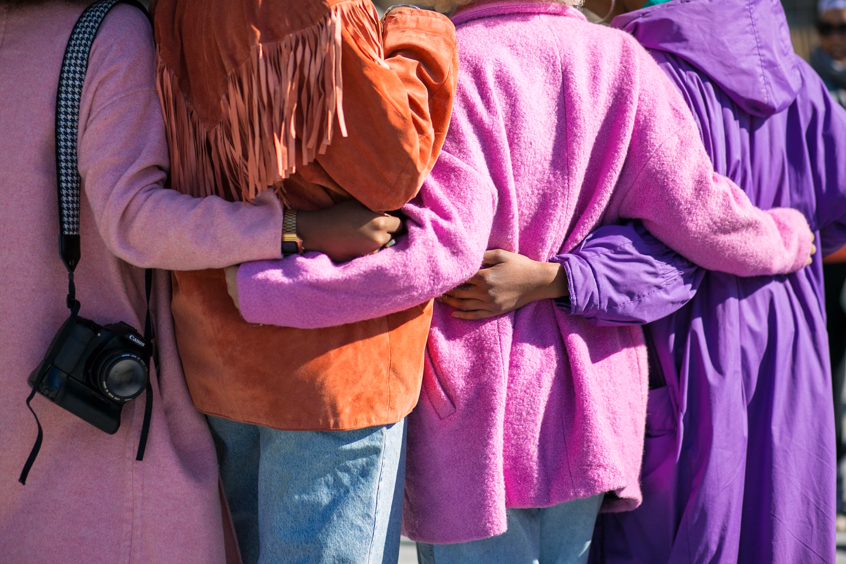 Four people standing side by side with arms around each other's waists in colorful jackets.