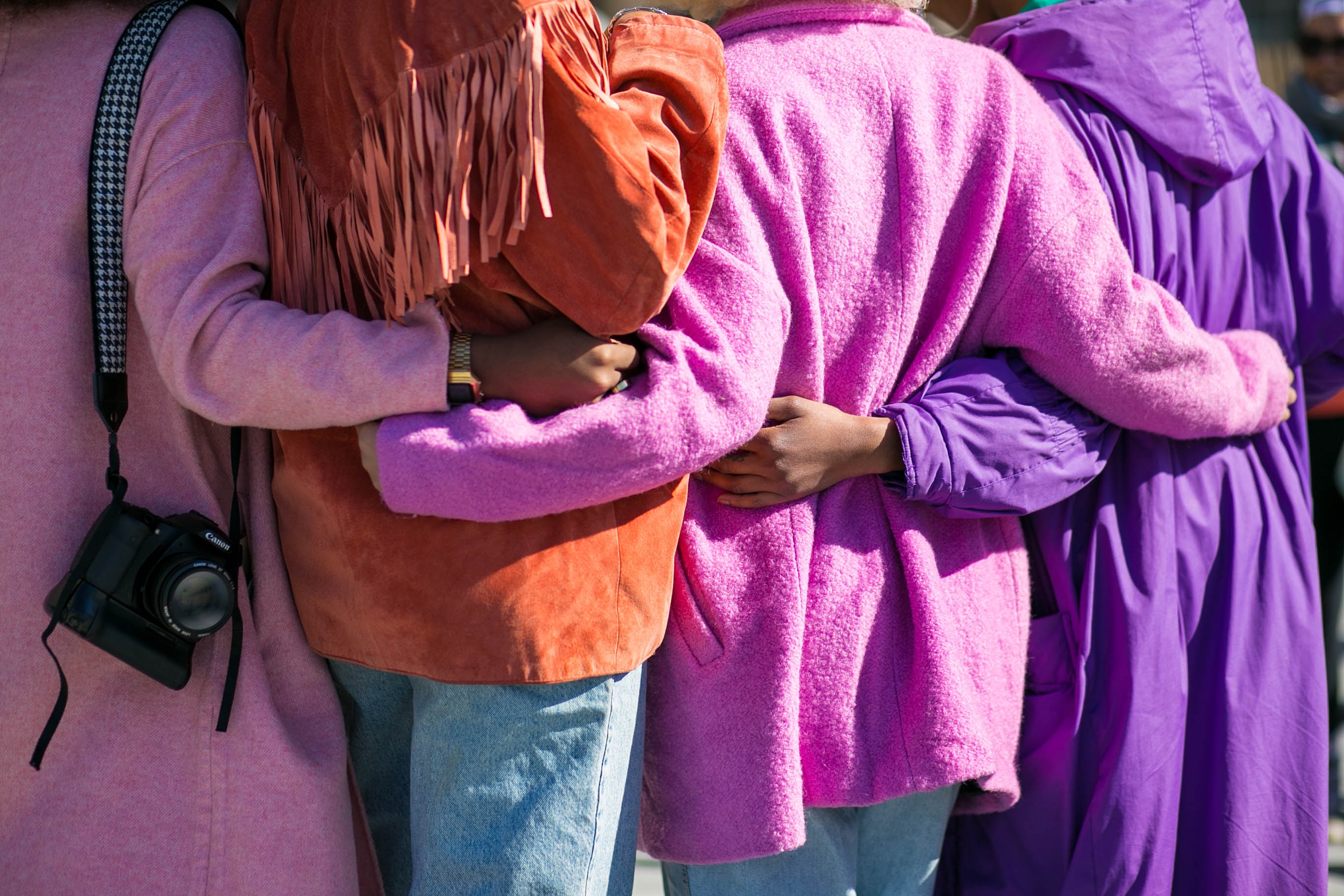 Four people standing side by side with arms around each other's waists in colorful jackets.