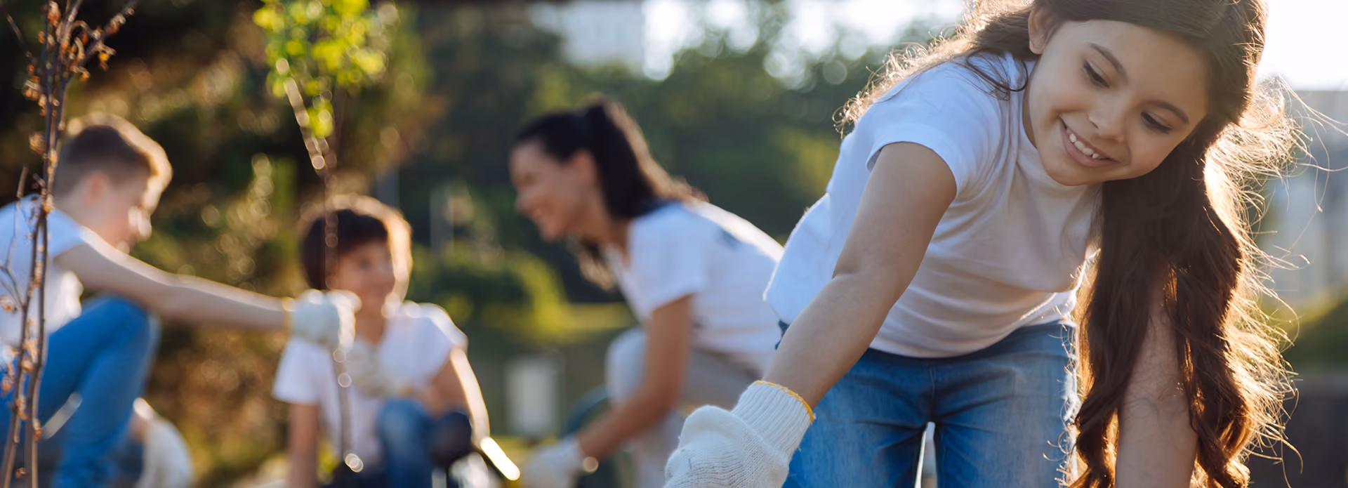 Smiling girl with long hair gardening outside with others blurred in background on a sunny day.