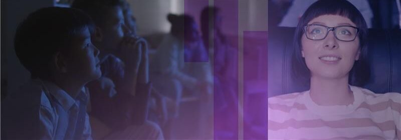 Smiling woman with glasses watching with children in dim light, purple overlay on image.