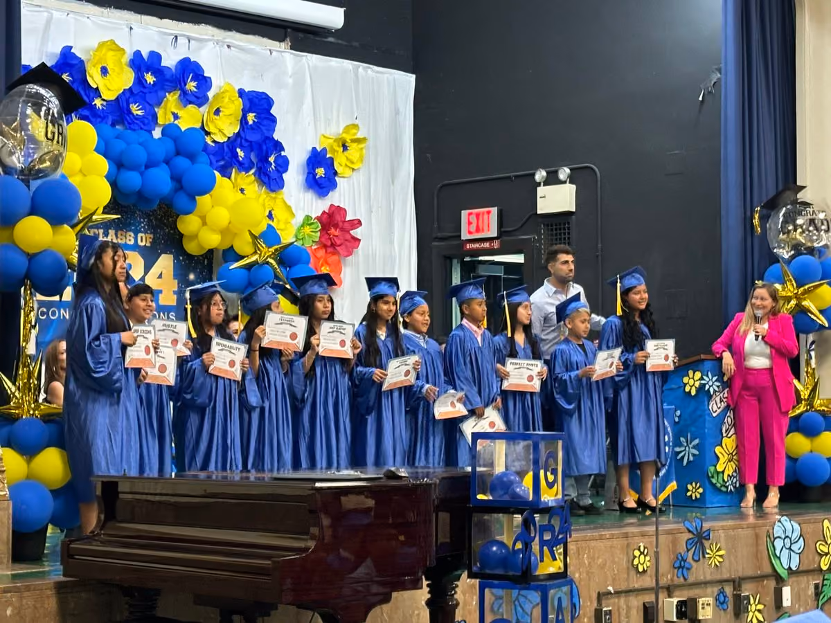 Students in blue caps and gowns holding certificates on graduation stage