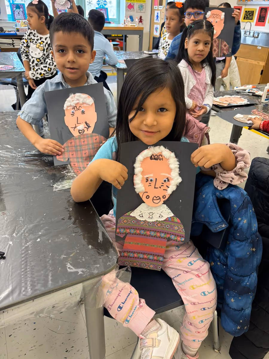 Students displaying handmade portrait artwork of elderly people in art class