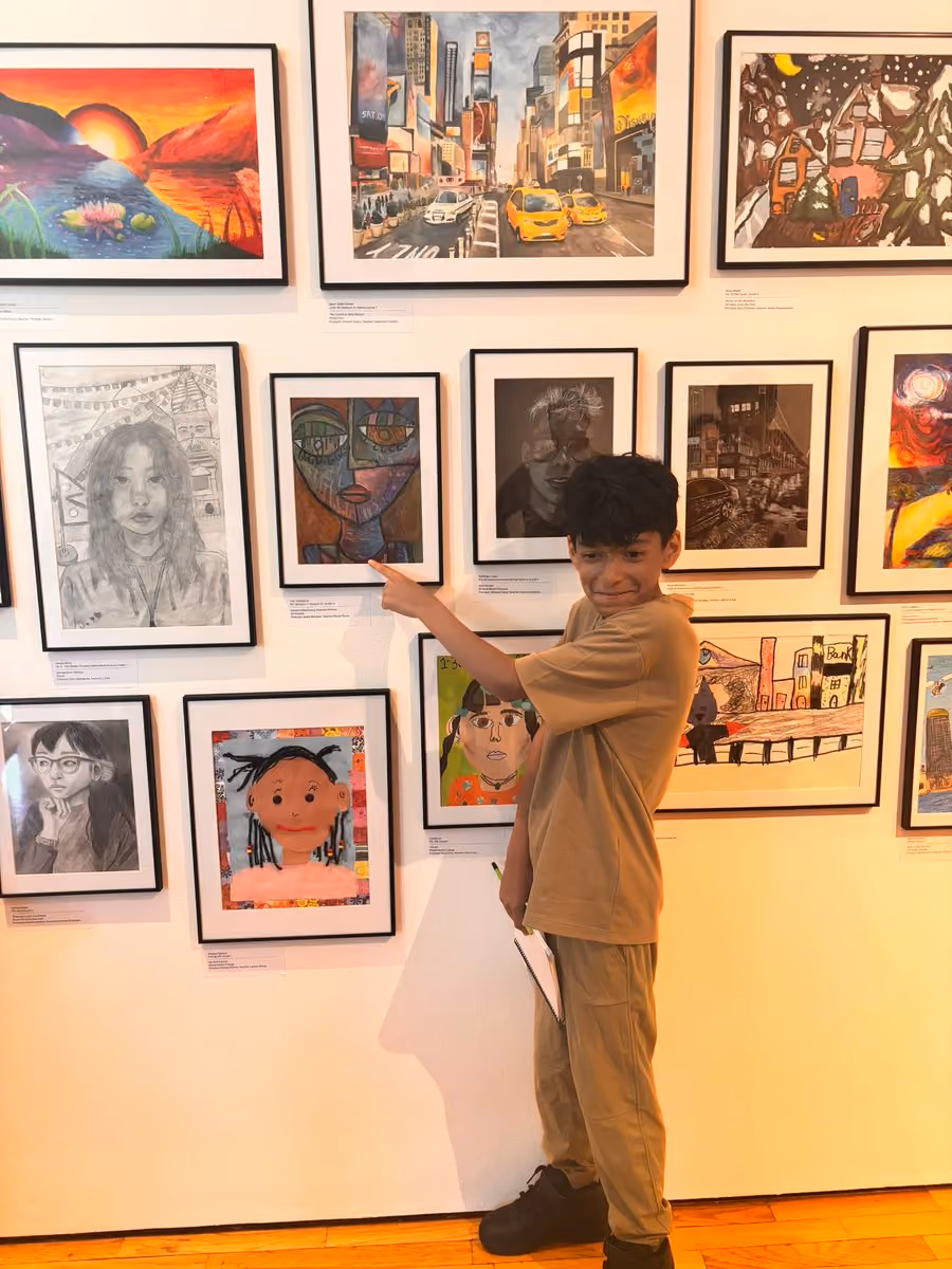 Student pointing proudly at their artwork in a school art exhibition
