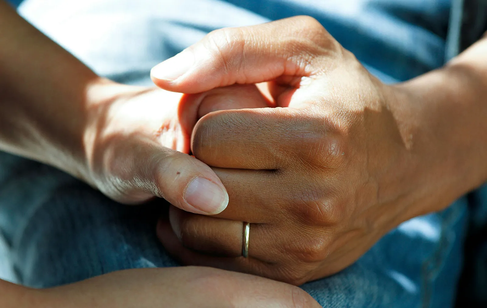 Close-up of two people's hands clasped together in a comforting gesture, one wearing a wedding ring.