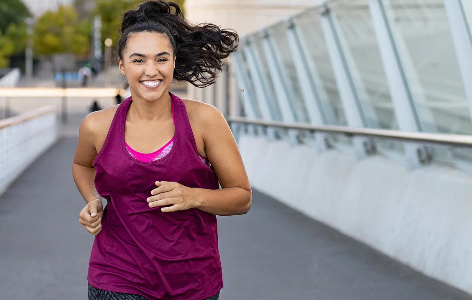 A woman smiling while jogging outdoors on a city walkway.