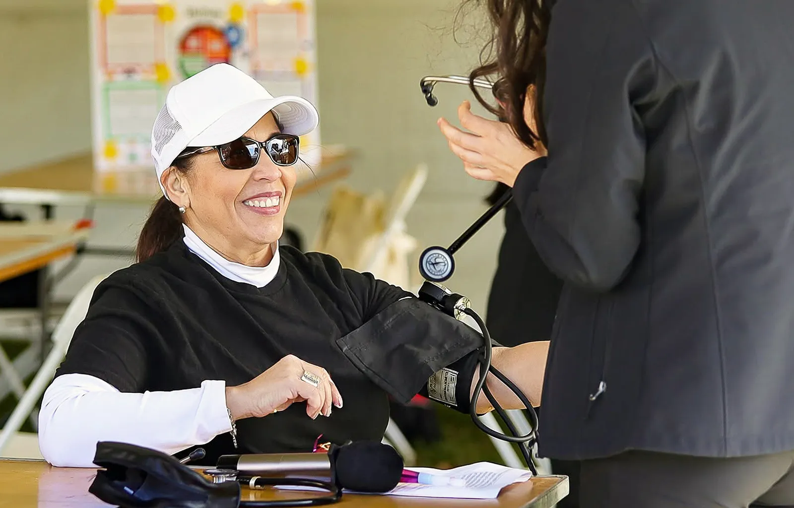 A woman smiling while having her blood pressure checked at an outdoor community health screening booth.