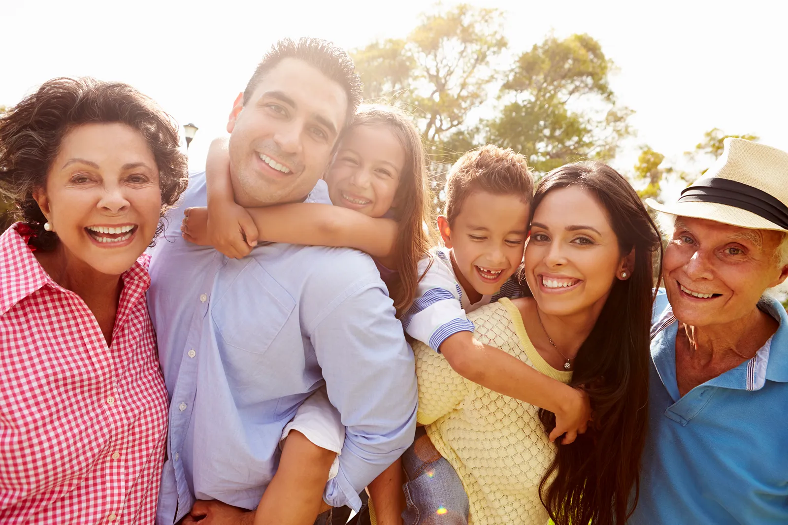 A multigenerational family of grandparents, parents, and children smiling together outdoors.