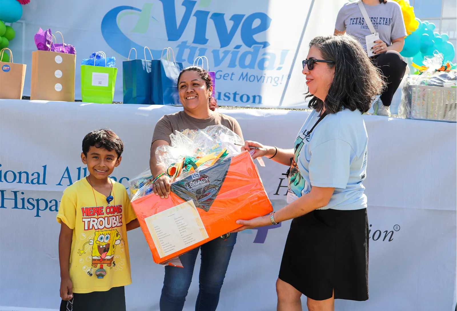 A mother and son receiving a gift basket on stage at a 'Vive tu vida' community health event in Houston.