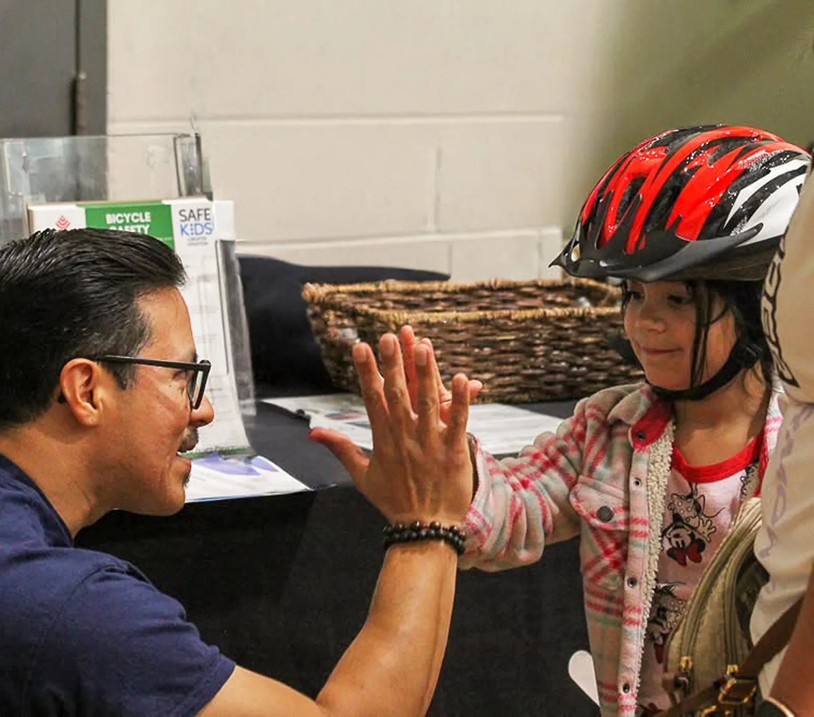 A man high-fiving a young girl wearing a bike helmet at a bicycle safety event.
