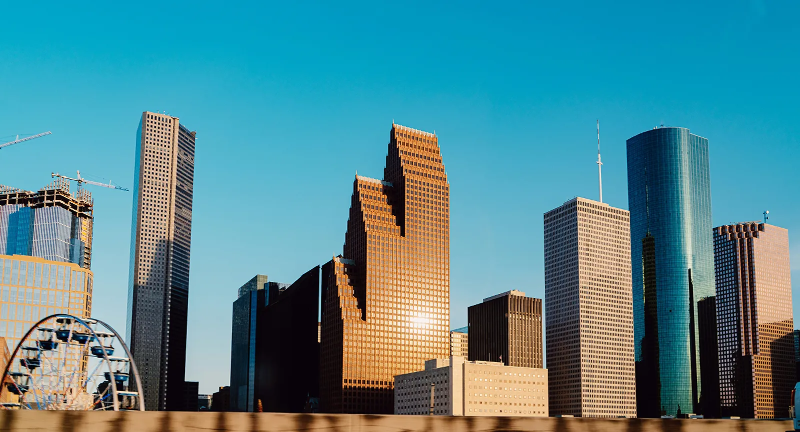 The downtown Houston skyline against a clear blue sky, with a Ferris wheel in the foreground.