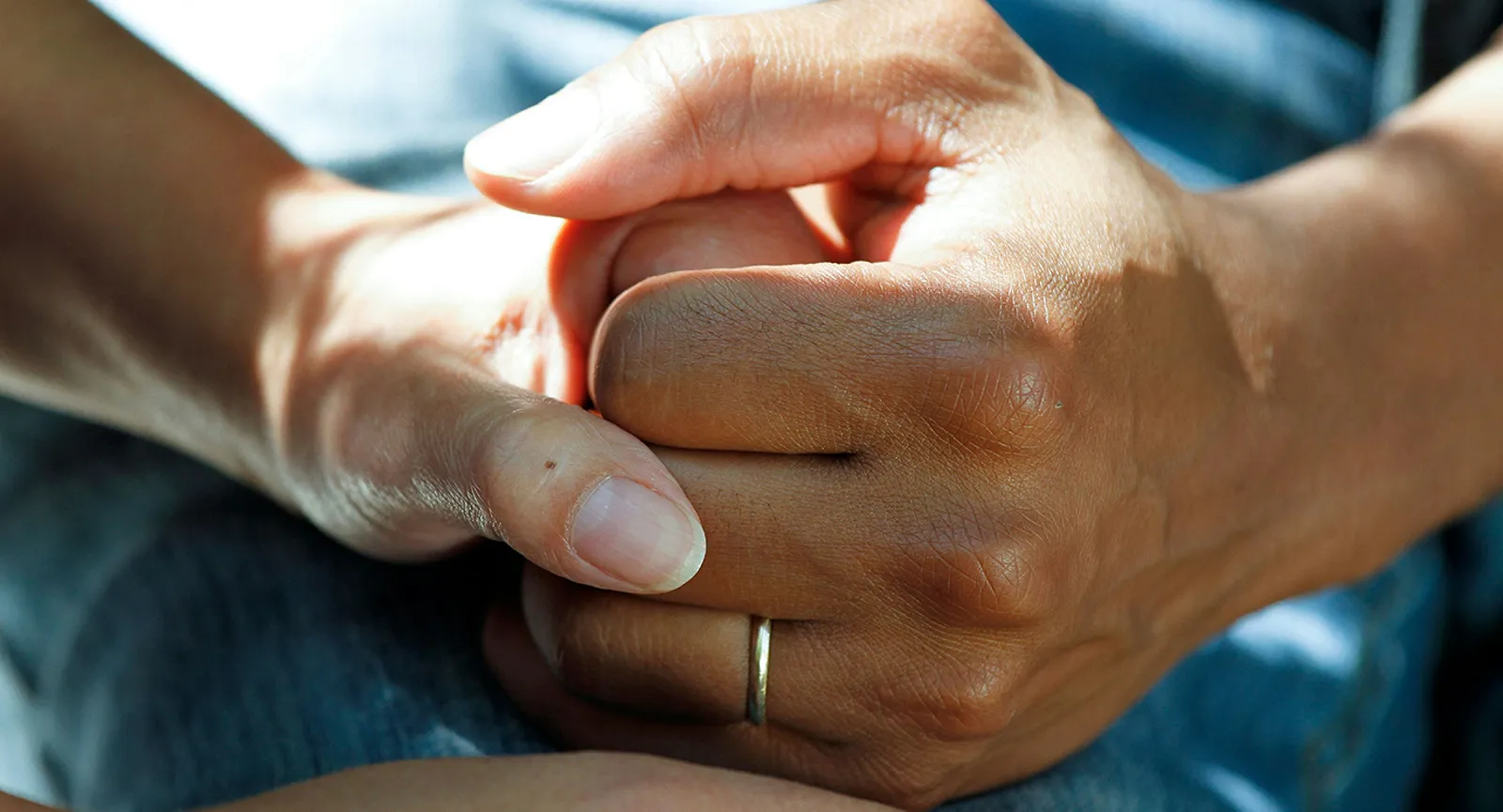 Close-up of two people's hands clasped together in comfort, one wearing a wedding ring.