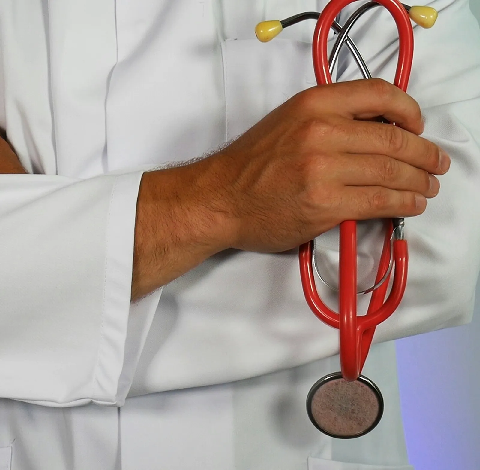 A healthcare provider in a white coat holding a red stethoscope.