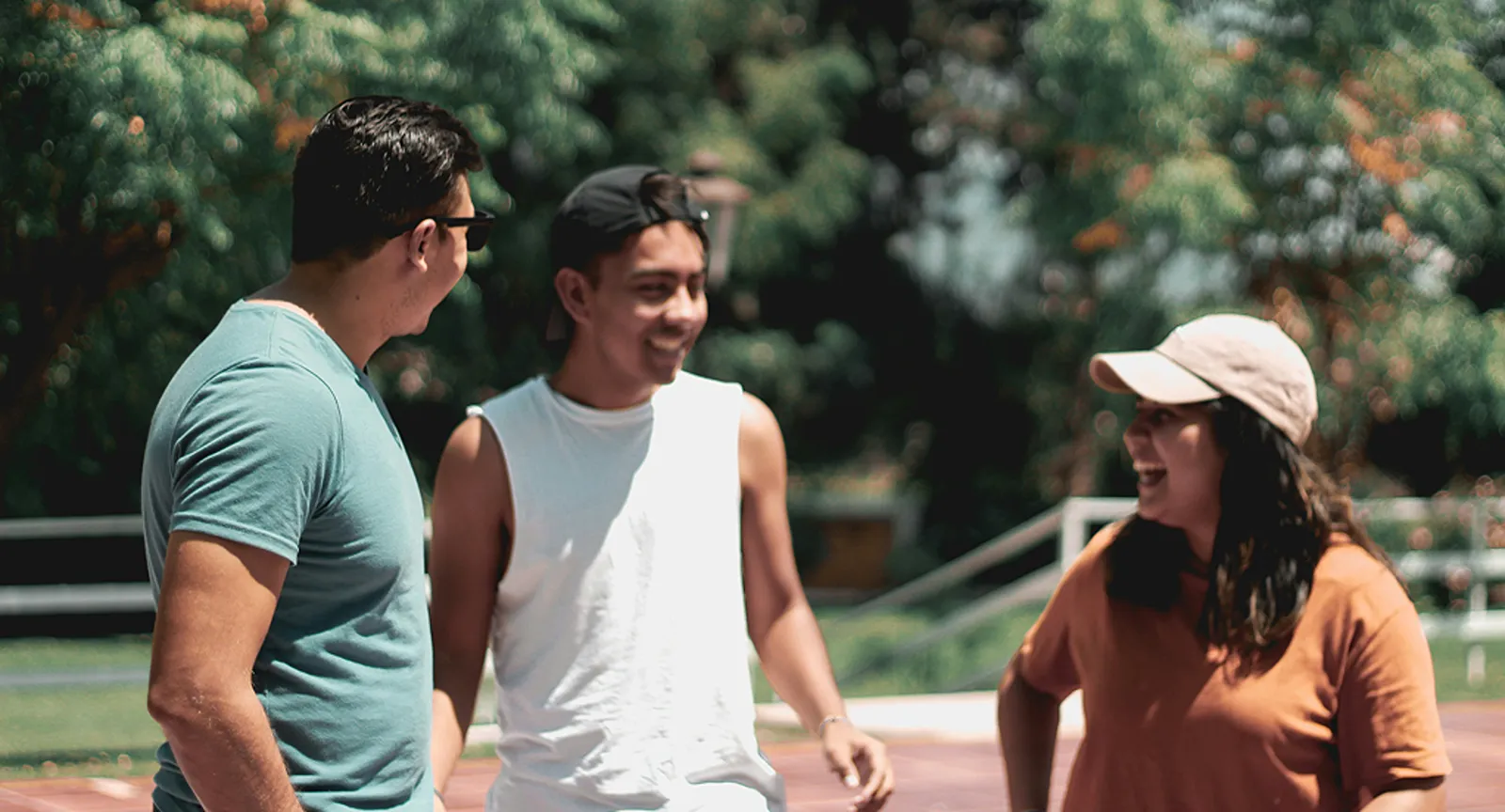 Three people laughing together outdoors on a walking track surrounded by trees.